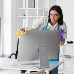A woman cleaning a large computer monitor in an office